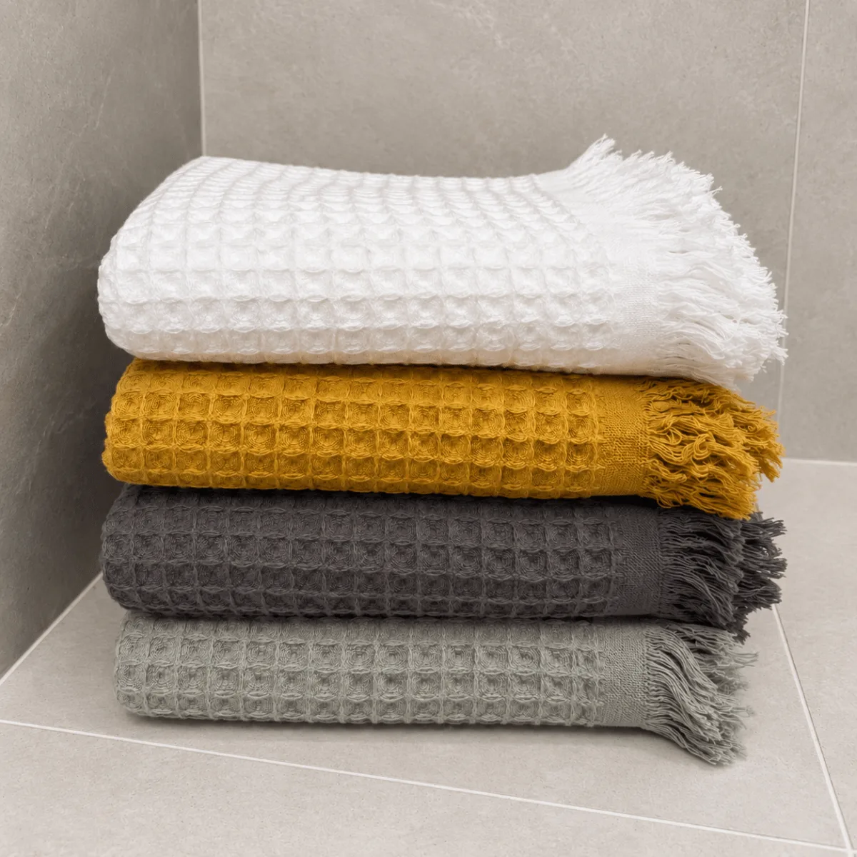 ręczniki waflowe ułożone jeden na drugim w czterech kolorach w łazience